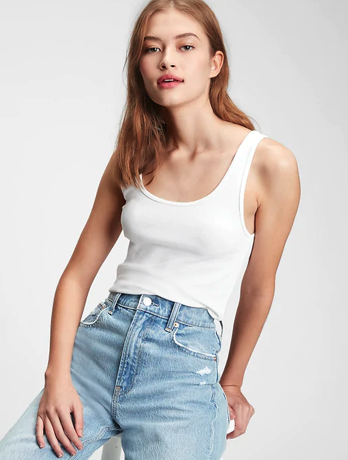 Model wearing white tank top with light wash blue jeans