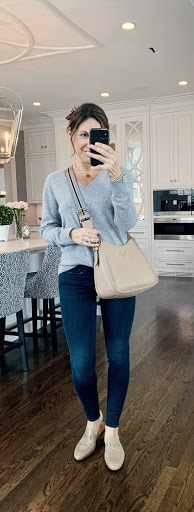 Alysia wearing a gray sweater, dark blue jeans, nude slip on shoes, and a nude crossbody bags