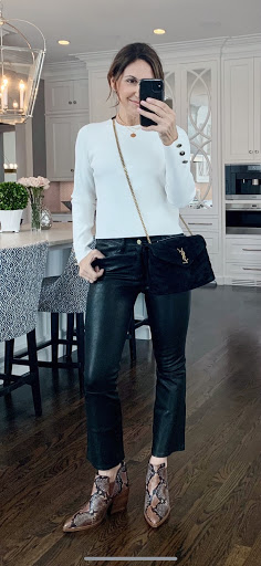 Alysia wearing a white sweater, black shiny pants, and snake print boots with a black crossbody bag