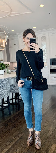 Alysia wearing a black sweater, blue jeans with a Gucci belt, snake print boots, and a black crossbody bag